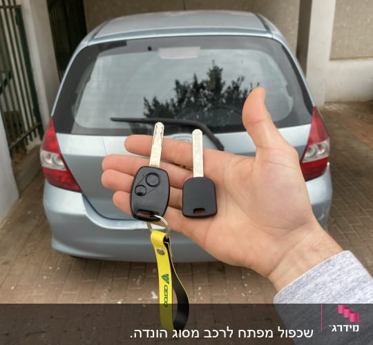 מפתחות רכב ביד מול מכונית חונה